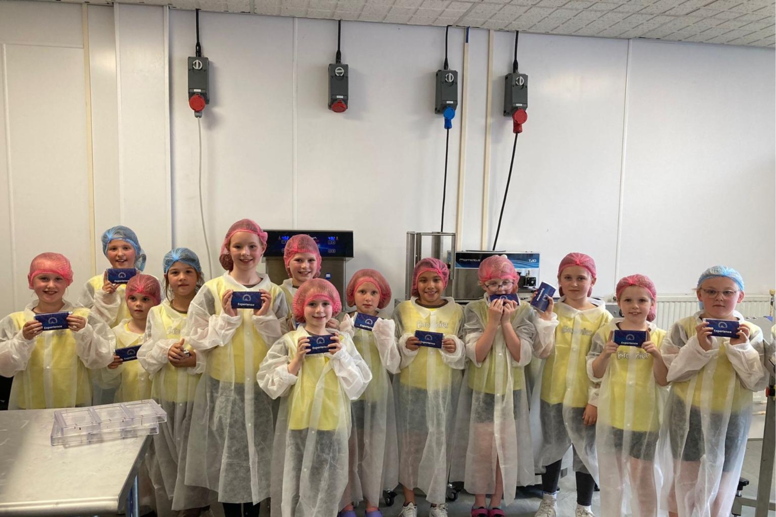 A school group in lab coats and hairnets inside the JJA Snack chocolate factory